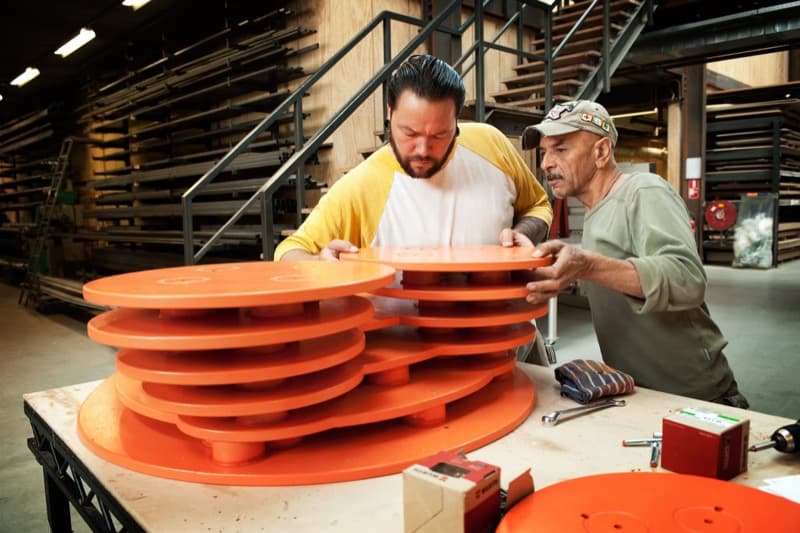 Twee makers tillen samen ronde tafelbladen op een werkbank in de werkplaats (voorbeeldfoto)